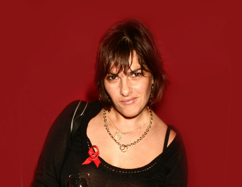 Portrait photo of tracey emin wearing ared bow on a dark red background 