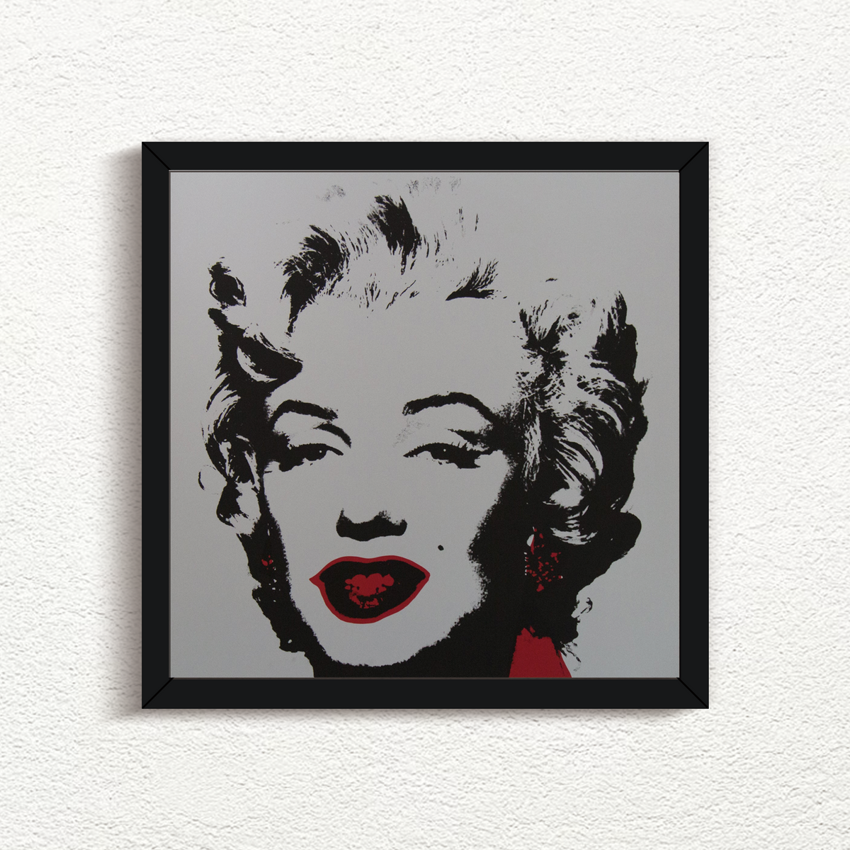 an image of an artwork titled 'golden marilyn 36' by andy warhol in a black frame. the artwork features a stencilled image of marilyn monroe's face in black on a grey background, with red pops of colour around the mouth and to the right of the face. this is a sunday b morning print