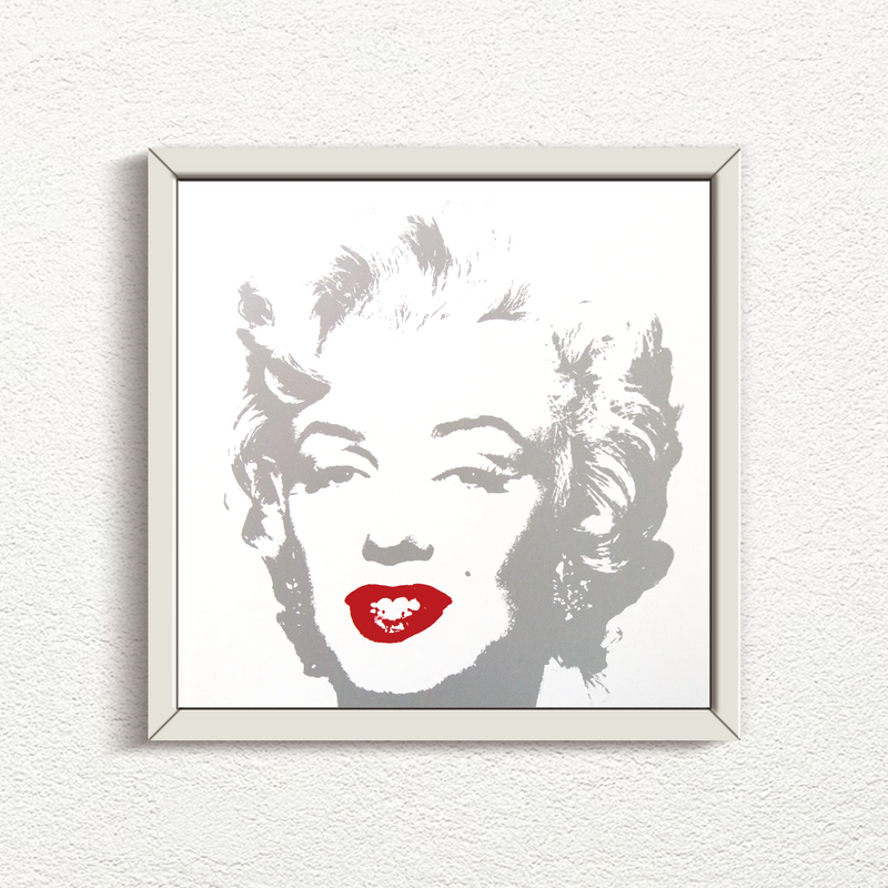 an image of an artwork by andy warhol titled 'golden marilyn 35' in a white frame. the artwork features a stencilled image of marilyn monroe's face in silver atop of a white background. the only pop of colour is on monroe's lips, which are in red. this is a sunday b morning print