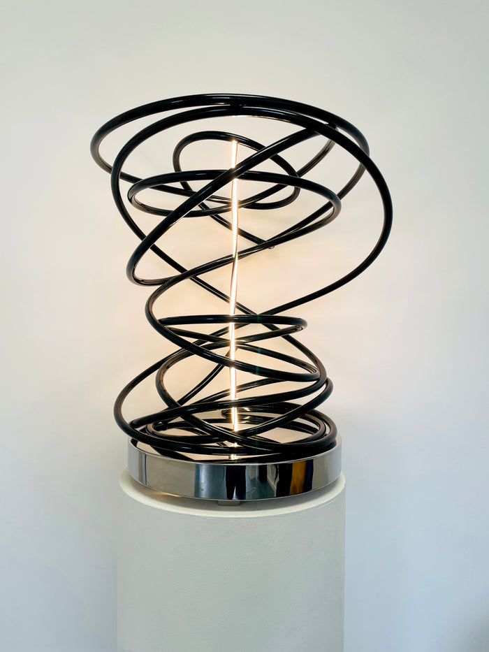 Illuminate your space with Mark Beattie's White in Tall Black Spiral, a unique sculpture featuring dimmable LED white light and painted copper on a mirror-polished stainless steel plinth. This one-of-a-kind masterpiece, measuring 67 x 54 x 52cm, is a captivating blend of light, texture, and contemporary design. Explore the artistic brilliance of White in Tall Black Spiral, available in different LED colors to suit your personal style and preferences.