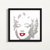 an image of an artwork by andy warhol titled 'golden marilyn 35' in a black frame. the artwork features a stencilled image of marilyn monroe's face in silver atop of a white background. the only pop of colour is on monroe's lips, which are in red. this is a sunday b morning print