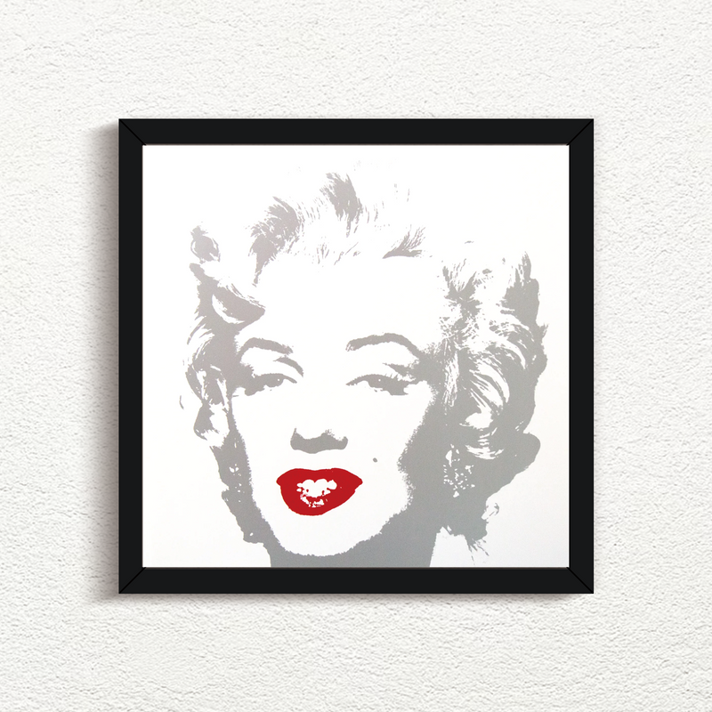 an image of an artwork by andy warhol titled 'golden marilyn 35' in a black frame. the artwork features a stencilled image of marilyn monroe's face in silver atop of a white background. the only pop of colour is on monroe's lips, which are in red. this is a sunday b morning print