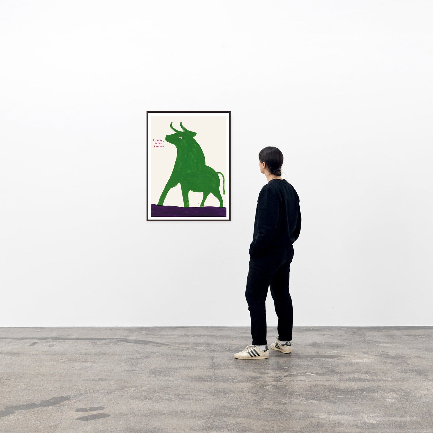 photo of a framed david shrigley art print hanging on a wall in a viewing space, with a single spectator to its right. the framed shrigley print itself features a deep green bull in an aggressive stance, with small text next to its mouth stating 'I WILL NOT FIGHT'. this david shrigley print features his signature cartoon-ish style and is on a beige background. the print is framed in a black box frame with a very small border. buy david shrigley prints