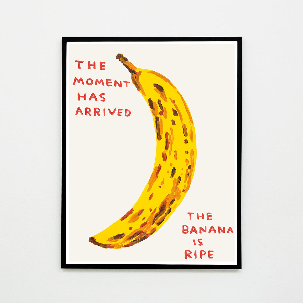 this is an image of a david shrigley artwork titled 'the moment has arrived' in a black frame. the artwork features a large painting of a brown spotted banana with handwritten text either side stating 'the moment has arrived', 'the banana is ripe'. this is a david shrigley print for sale