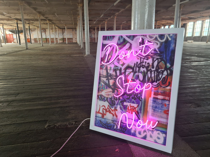 Infuse your space with creativity and energy with Tony Spink's Don't Stop Now. This one-of-a-kind artwork features purple neon on a graffiti canvas backing, elegantly presented in a white wooden frame. Measuring 65 x 85 cm, this original masterpiece is a unique fusion of neon art and urban flair. Elevate your space with this distinctive neon artwork, a dynamic addition to any art collection.