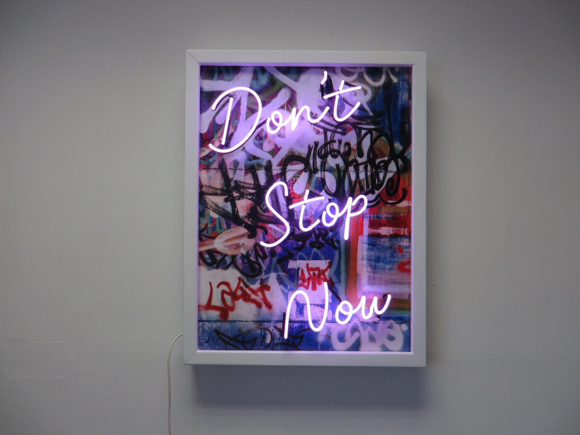 Infuse your space with creativity and energy with Tony Spink's Don't Stop Now. This one-of-a-kind artwork features purple neon on a graffiti canvas backing, elegantly presented in a white wooden frame. Measuring 65 x 85 cm, this original masterpiece is a unique fusion of neon art and urban flair. Elevate your space with this distinctive neon artwork, a dynamic addition to any art collection.