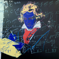 an image of an andy warhol artwork titled 'beethoven 390'. the image features beethoven colourised with a royal blue face, yellow hair and writing equipment, and a red scarf. the background is black, and there is an overlay of blue musical notation. this is a sunday b morning print