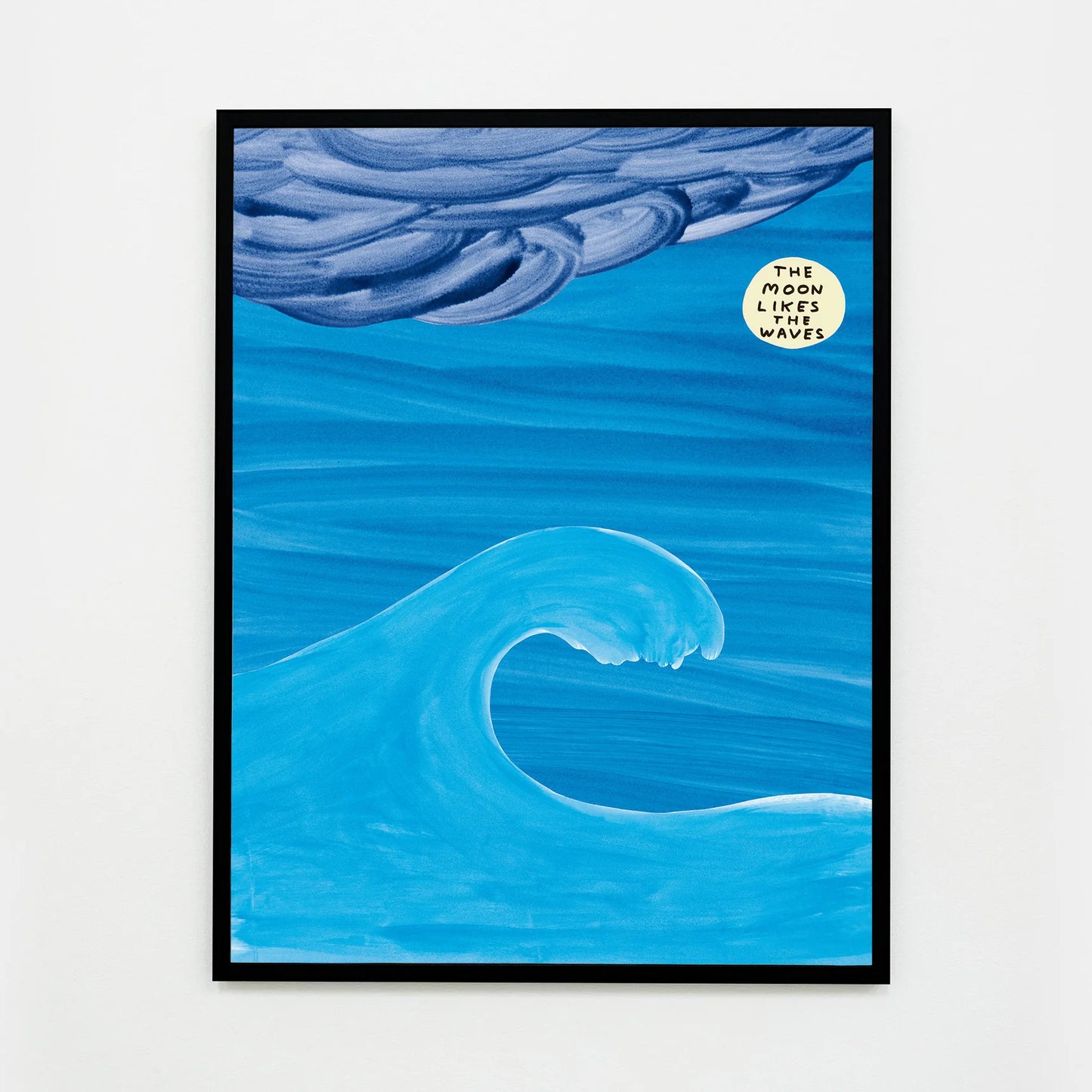 a photo of david shrigley print 'the moon', framed in a black frame, and featuring an ocean wave on a blue background and a stormy cloud, with a glowing moon, upon which the text 'the moon likes the waves' is written, all in shrigley's signature cartoonish and childlike style. David Shrigley prints, David Shrigley art prints, David Shrigley for sale, buy david shrigley prints, buy david shrigley posters, david shrigley posters for sale