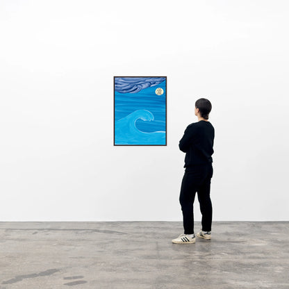 a photo of david shrigley print 'the moon', framed in a black frame and hung on a wall, with a spectator viewing the piece. the piece features an ocean wave on a blue background and a stormy cloud, with a glowing moon, upon which the text 'the moon likes the waves' is written, all in shrigley's signature cartoonish and childlike style. David Shrigley prints, David Shrigley art prints, David Shrigley for sale, buy david shrigley prints, buy david shrigley posters, david shrigley posters for sale