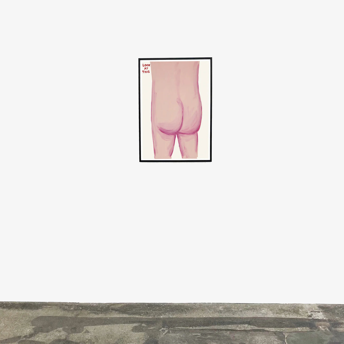 Image of an artwork by David Shrigley titled 'Look at This' in a black frame, hung on a white wall. The piece features the bare bottom of someone, with the tagline 'look at this' in the top left. this is a david shrigley poster and a david shrigley print