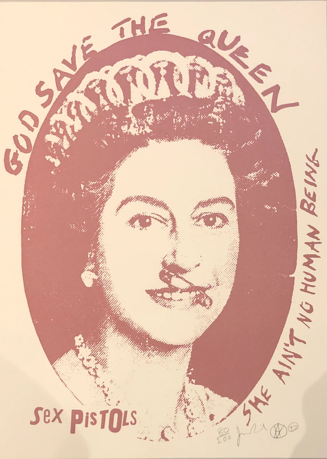 an image of a jamie reid artwork titled god save the queen, which features a red screenprint of queen elizabeth on a white background, in which queen elizabeth has a safety pin through her mouth and states 'GOD SAVE THE QUEEN SHE AIN'T NO HUMAN BEING', with the sex pistols logo at the lower left, and jamie reid's signature on the lower right